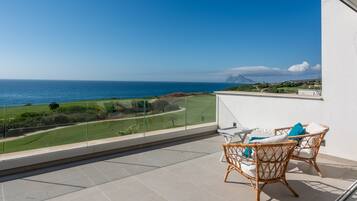 Ein Balkon mit Blick auf das Meer, Korbmöbel und eine weiße Wand.