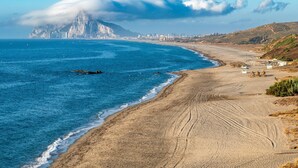 Een kuststrand met een berg op de achtergrond, heldere lucht en een zandstrand.