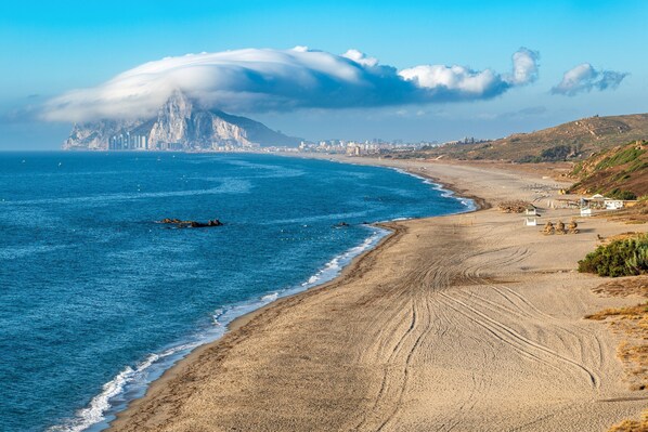 Una playa costera con una montaña al fondo, cielos despejados y una orilla arenosa.