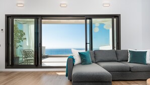 Een moderne woonkamer met een grijze modulaire bank, een ronde salontafel en uitzicht op de oceaan door grote schuifdeuren.