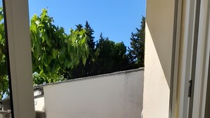 On aperçoit, à travers une porte-fenêtre coulissante, un jardin avec une piscine, une terrasse en bois et un mur blanc.