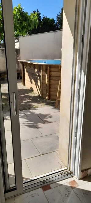 A view through a sliding glass door into a backyard with a pool, wooden deck, and a white wall. - Holiday Home 'L'Oustau De Maître Potager' with Private Terrace, Private Garden and Wi-Fi (Valréas)