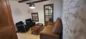 Un salon comprenant un canapé, deux fauteuils noirs, une table basse en bois, un luminaire suspendu et une porte en bois avec un panneau de verre.