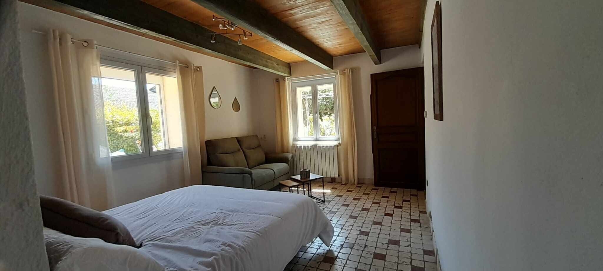 A bedroom with a bed, a chair, a small table, and a window.