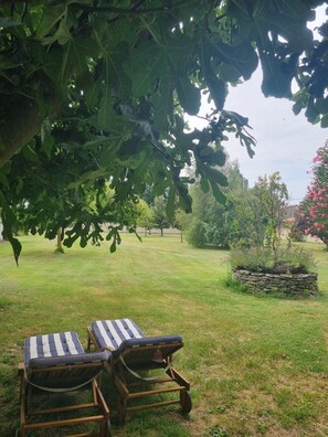Two wooden lounge chairs with striped cushions in a grassy outdoor area, surrounded by trees and a stone planter. - Holiday Home 'L'Oustau De Maître Potager' with Private Terrace, Private Garden and Wi-Fi (Valréas)
