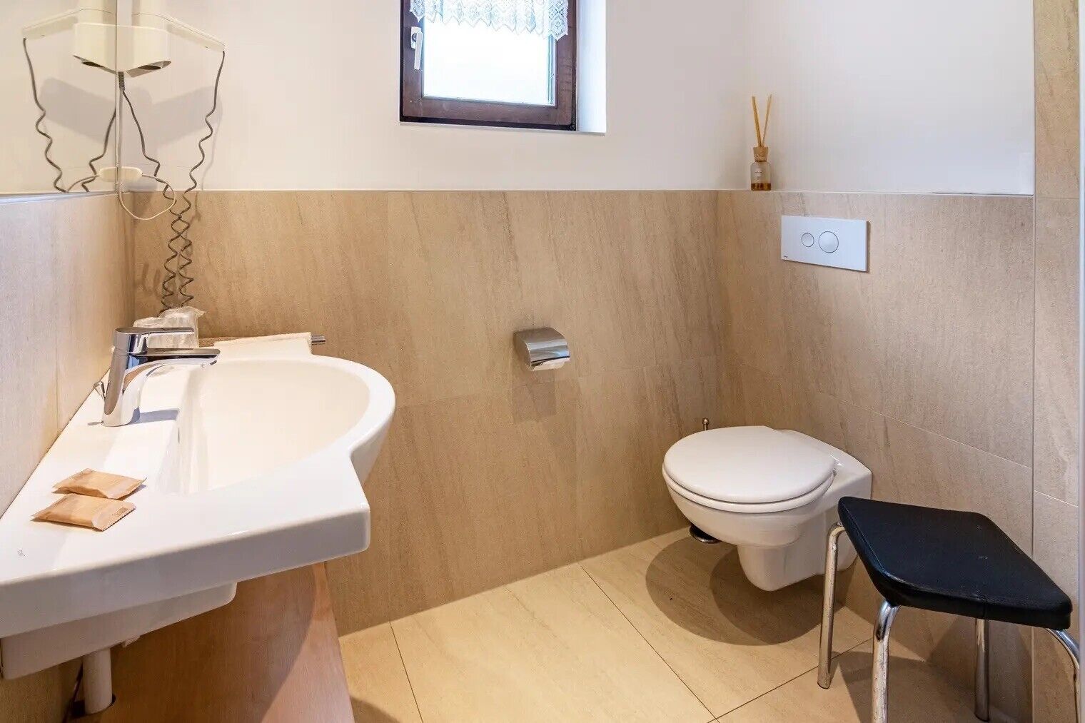 Ein Badezimmer mit einem weißen Waschbecken, einer Toilette und einem kleinen schwarzen Hocker.