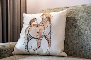 Un coussin orné d’une illustration de cheval, posé sur un canapé à la texture particulière.