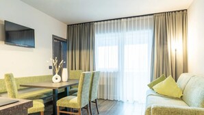 A hotel room with a dining table, chairs, a sofa, a flat-screen TV, and a large window with curtains. - Apartment 'Martellerhof - Opis Pennhaus Small' with Sea View, Shared Terrace and Wi-Fi (Martell)