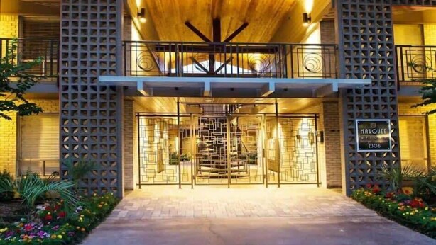 A modern building with a wooden facade, a central entrance with a geometric design, and a balcony with a railing.