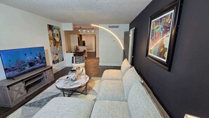 A modern living room with a flat-screen TV, a sofa, a coffee table, and artwork on the walls.