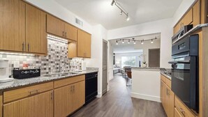 A modern kitchen with wooden cabinets, a granite countertop, and a coffee machine.