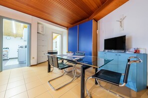 Une cuisine moderne avec une table en verre, des chaises noires, un meuble bleu et un téléviseur.