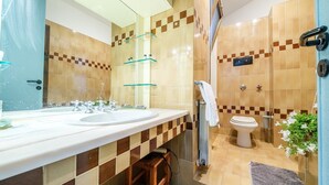 Ein modernes Badezimmer mit einem Doppelwaschtisch, einer Duschkabine aus Glas, einer Toilette und einer kleinen Stehgehilfe.