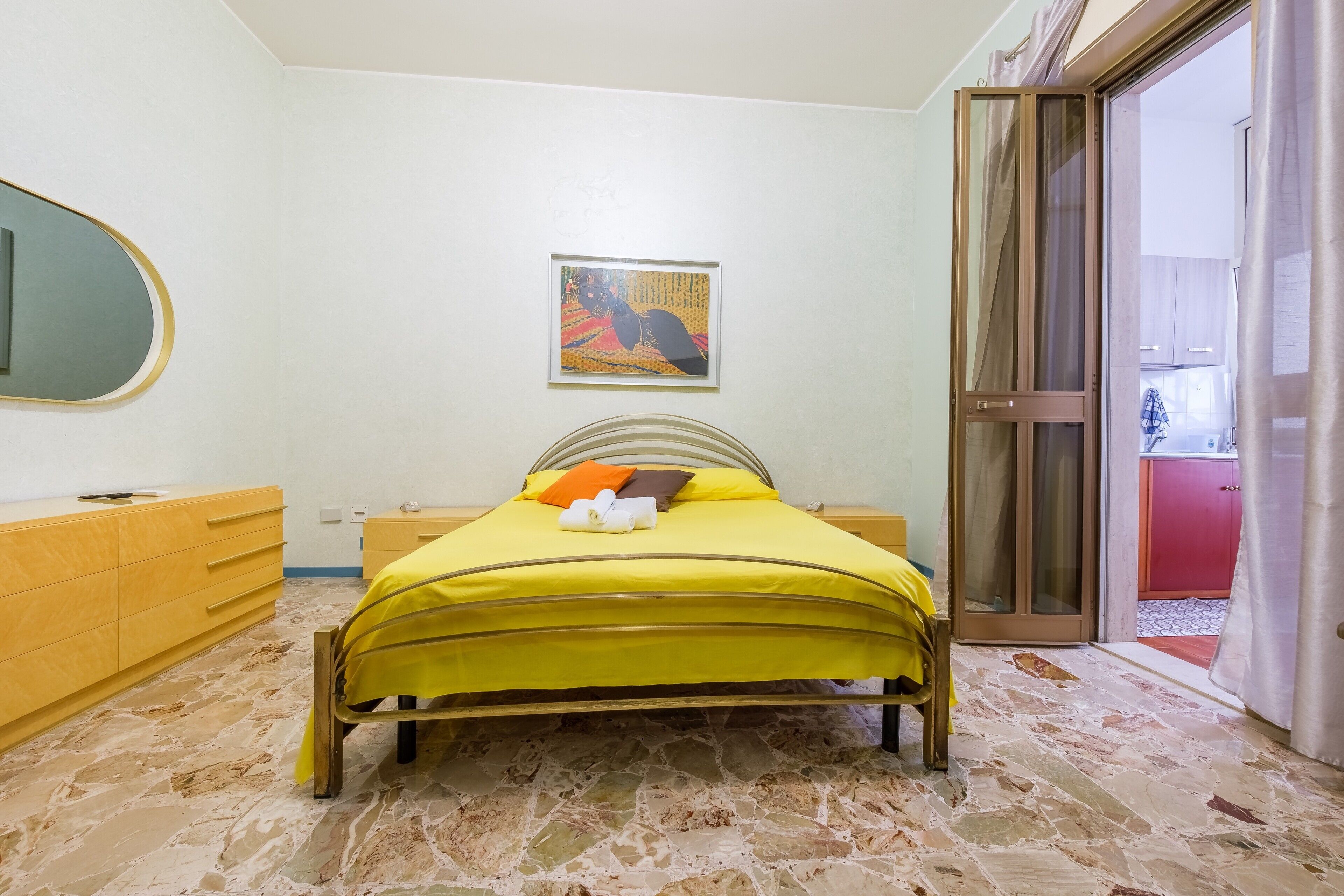 A bedroom with a bed, a dresser, a mirror, a framed picture on the wall, and a sliding glass door leading to another room.
