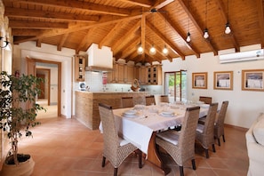 A dining area with a wooden ceiling, a kitchen in the background, and a dining table set for four.