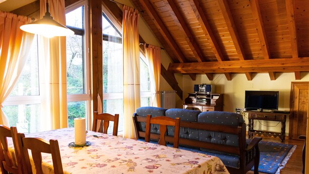 Una zona menjador amb taula preparada per a dues persones, un sofà i una televisió en una habitació amb bigues de fusta.