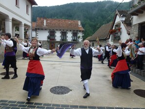 Una actuación de danza tradicional en una plaza de pueblo, con edificios de piedra y montañas al fondo.