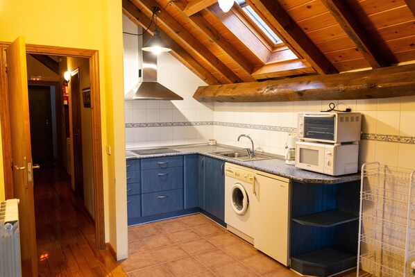A kitchen with wooden beams, a washing machine, a microwave, and a sink.