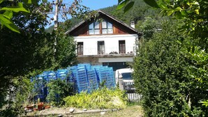 Una casa de dues plantes amb un balcó, envoltada de vegetació i materials de construcció.