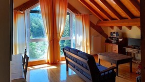 Habitació amb sostre de fusta, un sofà, una taula i vista a la vegetació exterior.