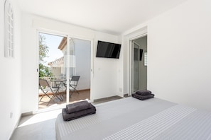 A bedroom with a bed, a TV, and a sliding glass door leading to an outdoor area with a table and chairs.