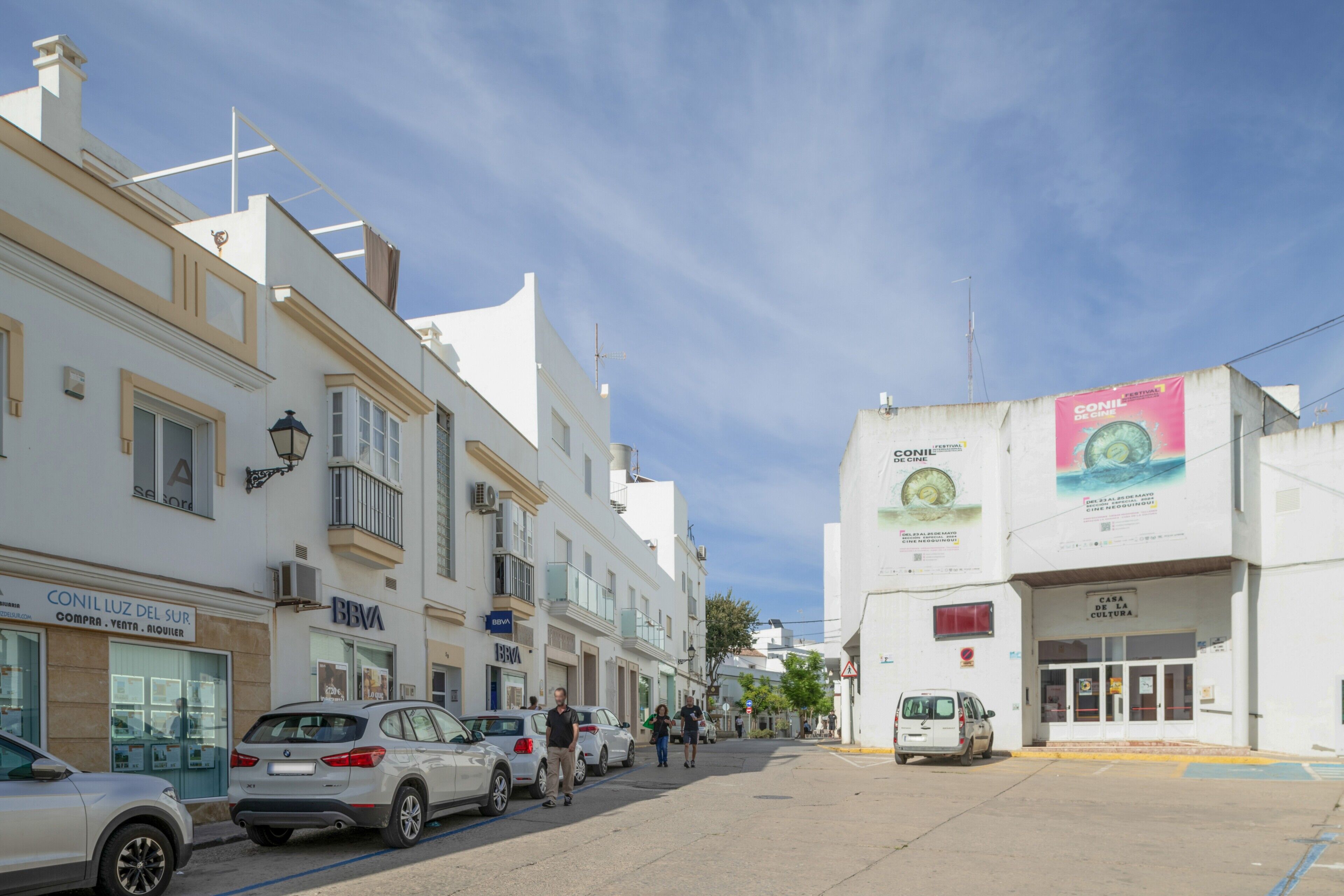 Rua com edifícios, carros estacionados e céu claro.