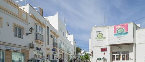 Rua com edifícios, carros estacionados e céu claro.