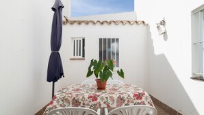 Un pequeño patio con una mesa, sillas, una planta en maceta y un paraguas azul.