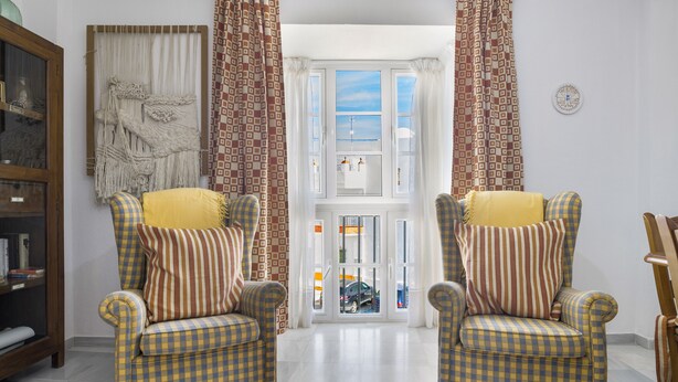 Una habitación con dos sillones a cuadros, un tapiz de macramé y vistas a un baño a través de una puerta.