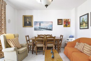 A living room with a dining table, chairs, a sofa, and various framed artworks on the walls.