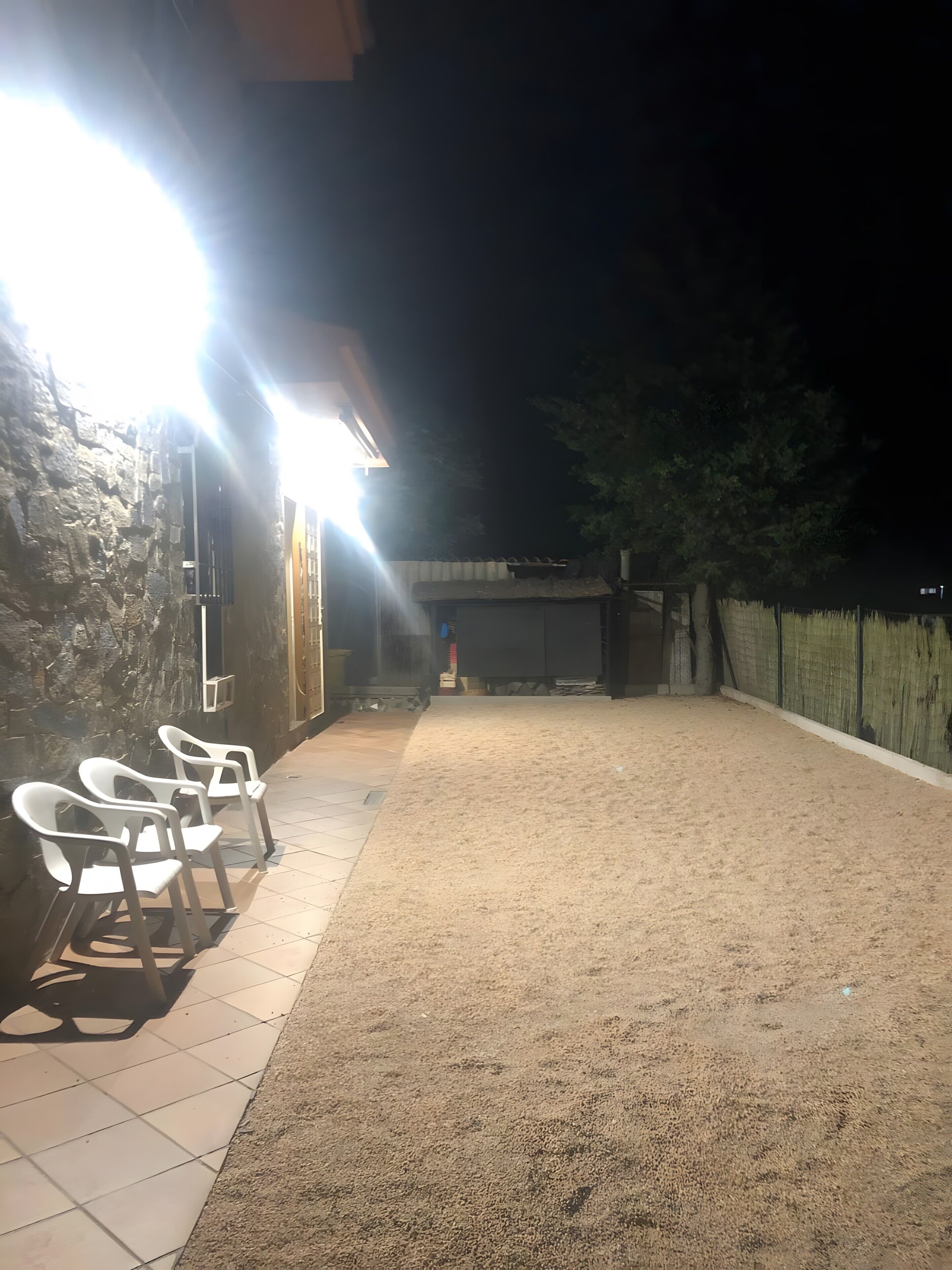 A patio with chairs, a stone wall, and a building with a bright light.