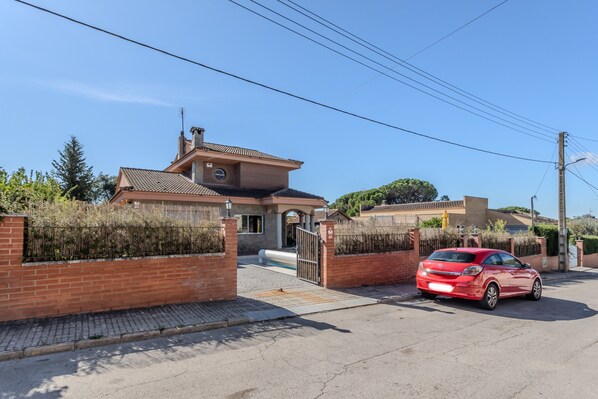 A residential house with a gated driveway, a red car parked in front, and a clear blue sky.