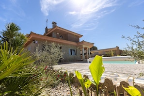 A house with a swimming pool, surrounded by a garden with various plants and a stone pathway.