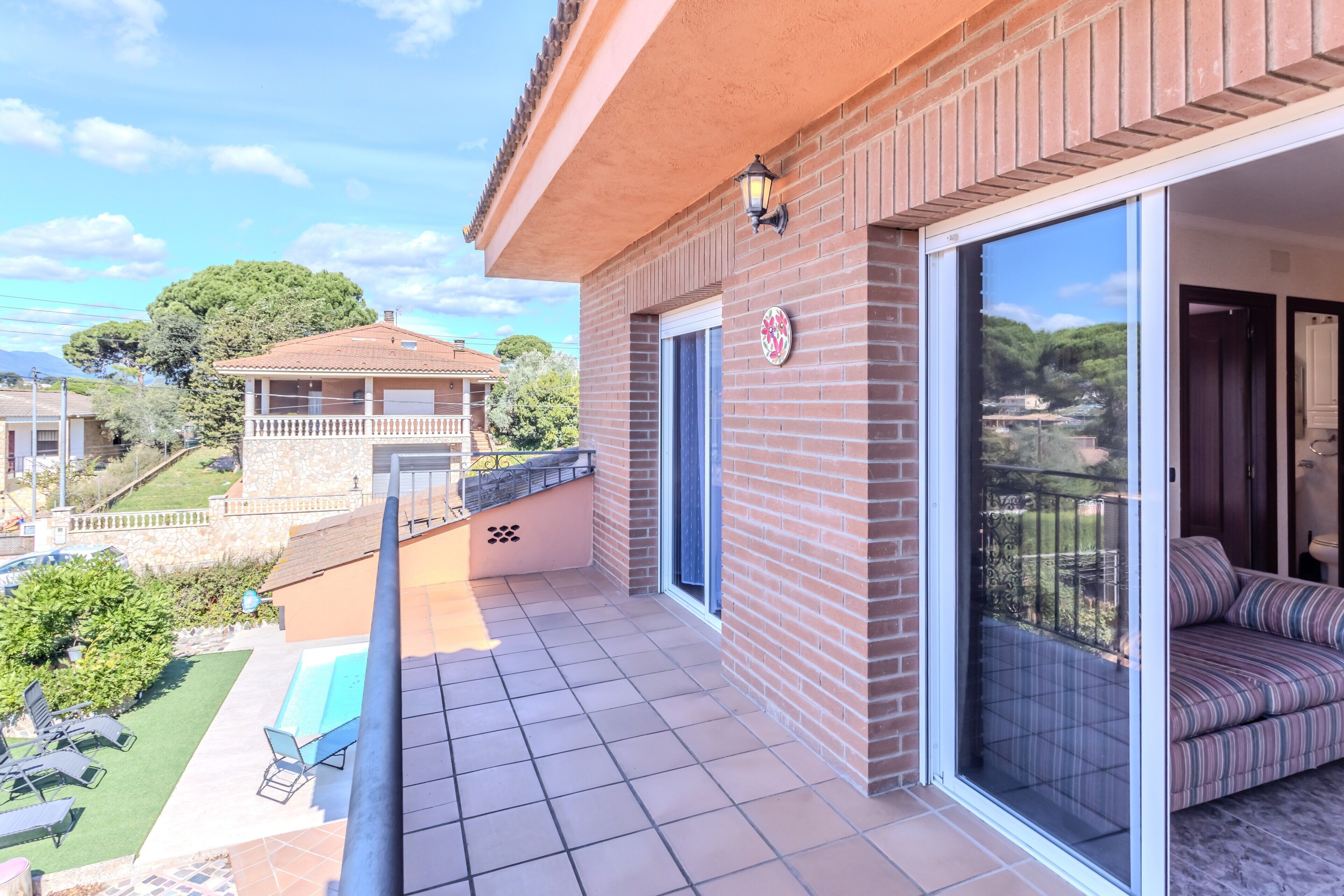 A balcony with a view of a garden and a neighboring house, a sliding glass door, and a patio area with outdoor furniture.