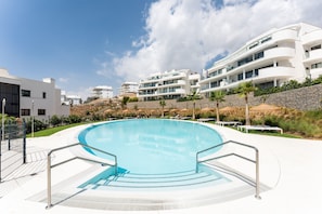 A swimming pool with a white deck, surrounded by modern buildings and a clear sky. - Stunning Sea View Apartment in Higueron West (Málaga)
