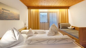 Een hotelkamer met een houten plafond, een bed met opvallende kussens, een bank met een kussen, en een groot raam met gordijnen.