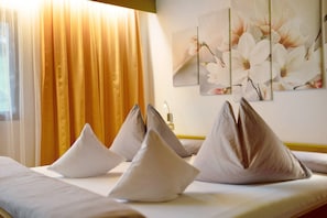 Une chambre d’hôtel avec un lit, des oreillers, une fenêtre avec des rideaux et un mur orné d’un tableau représentant des fleurs.