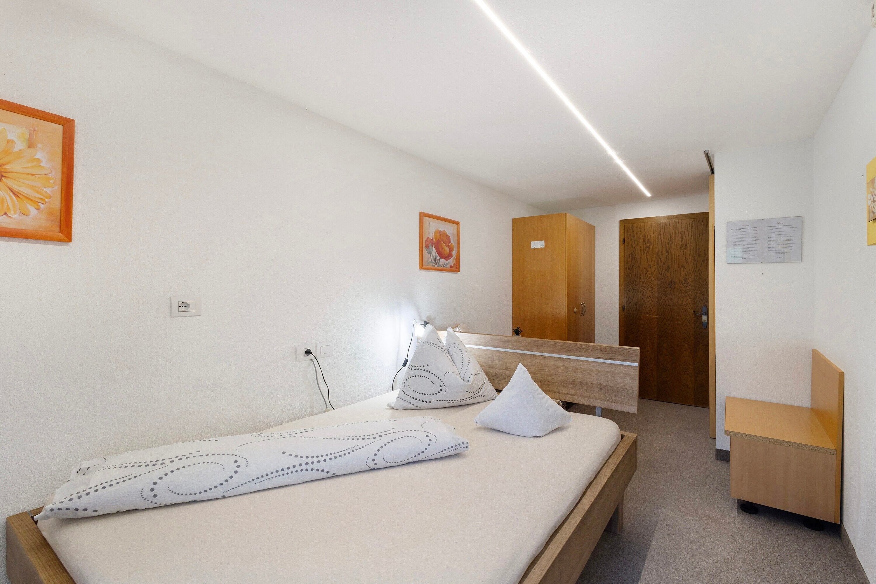 Una habitación de hotel con cama, mesita de noche, armario de madera y espejo.