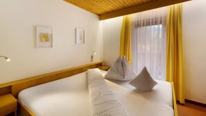A hotel room with a wooden ceiling, a bed with white bedding, two wall-mounted light fixtures, and a window with yellow curtains. - Room 'Ederhof 7' with Mountain View, Shared Terrace, Wi-Fi, and Breakfast Included (Ahrntal - St.Peter)