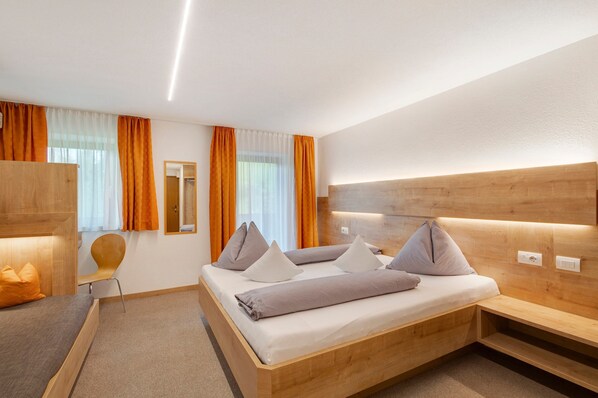A modern hotel room with a wooden bed, a bench, a chair, and a mirror.