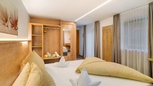 A hotel room with a bed, a wooden wardrobe, a mirror, and a window with curtains. - Room 'Ederhof 5' with Mountain View, Shared Terrace, Wi-Fi, and Breakfast Included (Ahrntal - St.Peter)