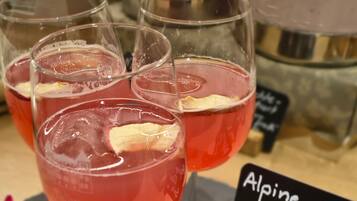 Un tavolo con quattro bicchieri di una bevanda rossa, un cartello con la scritta 'Alpine Glow Spritz' e fiori decorativi.