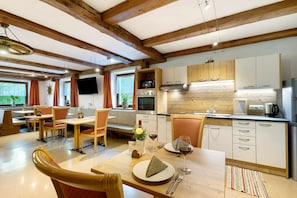 A modern kitchen with wooden beams, a dining area with chairs and a table, and a TV mounted on the wall.