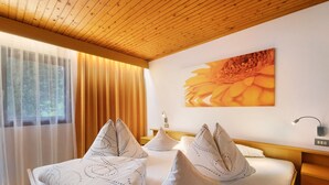 Habitació d'hotel amb sostre de fusta, un llit gran amb almoinades estampades, una tauleta de nit, una làmpada penjada a la paret i una finestra amb cortines.
