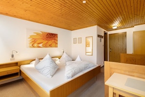 A bedroom with a wooden ceiling, a bed with patterned pillows, a nightstand, a bedside table, and a mirror.