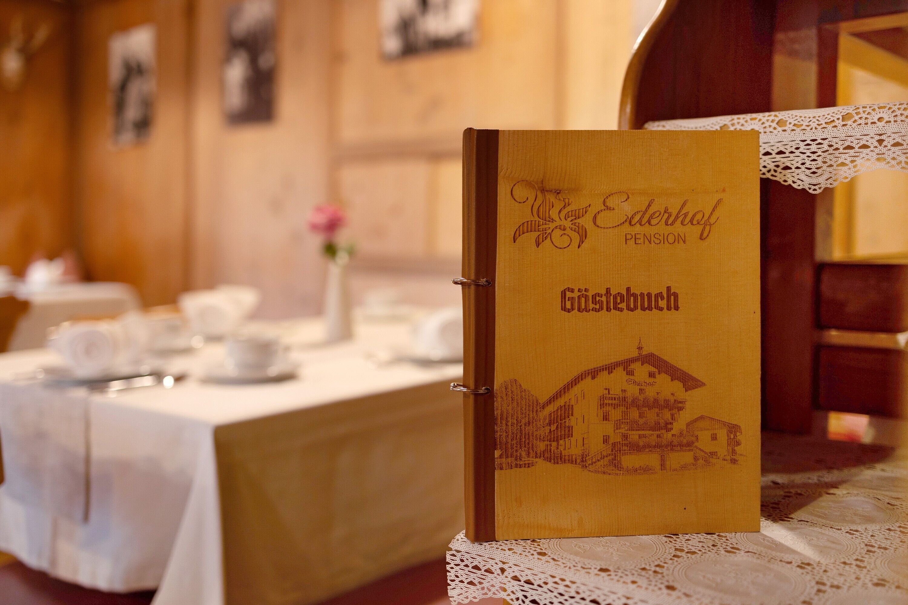 Uma pasta de madeira com os dizeres 'Ederhof Pension' e 'Gästehaus' em relevo, colocada sobre uma mesa com toalha de renda.