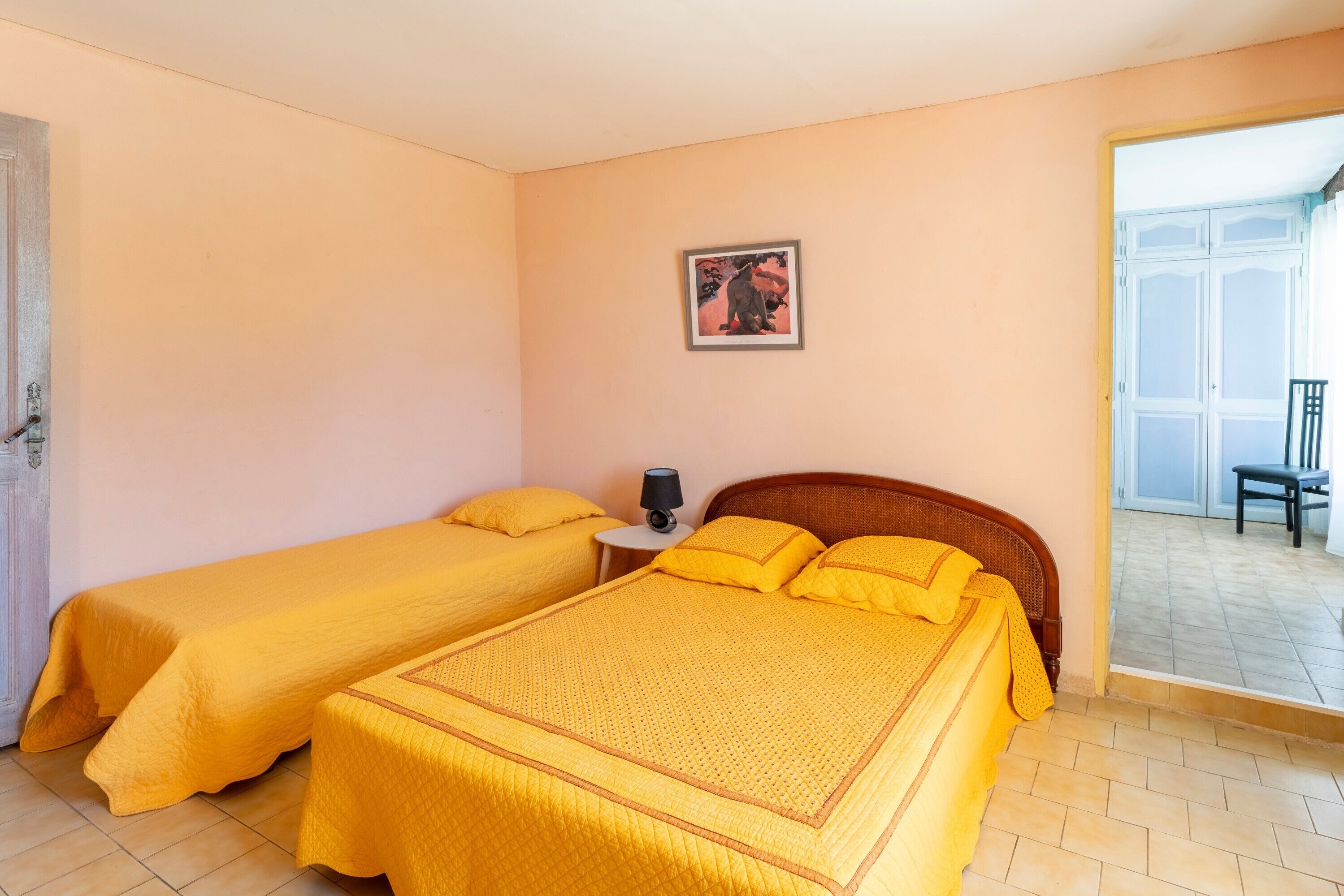 Una habitación con dos camas, una mesita de noche con una lámpara, un cuadro en la pared y vistas al exterior.