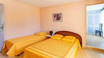 Una habitación con dos camas, una mesita de noche con una lámpara, un cuadro en la pared y vistas al exterior.