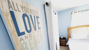 A bedroom with a bed, a nightstand, a wall with a motivational quote, and a white curtain. - Relaxing Beach Home Only 3 Miles From Beach! (Fort Pierce)