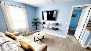 A living room with a sofa, a coffee table, a TV mounted on the wall, and a potted plant. - Relaxing Beach Home Only 3 Miles From Beach! (Fort Pierce)